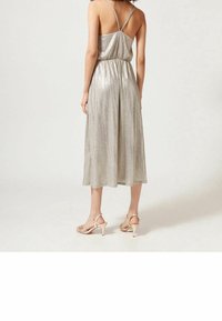 Silver metallisk midi-klänning med justerbara axelremmar och en samlad midja. Tyget har en ribbad textur, i kombination med nude strappy klackar.