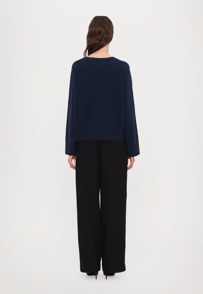 Navy blue knit sweater with ribbed hem, paired with wide-leg black trousers. Soft texture and relaxed fit, viewed from the back.