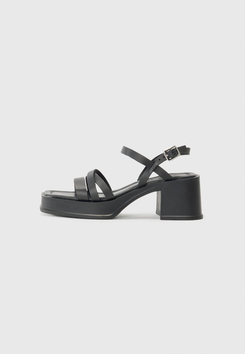 Sandalias negras de tacón con múltiples correas estrechas y punta redonda. El tacón tiene forma de bloque y una textura suave. Cierre con hebilla ajustable.