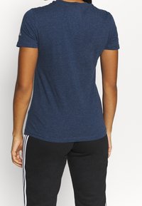 Granatowa koszulka z krótkim rękawem i okrągłym dekoltem, o miękkiej fakturze, z delikatnym melanżowym wzorem. Połączona z czarnymi spodniami sportowymi.