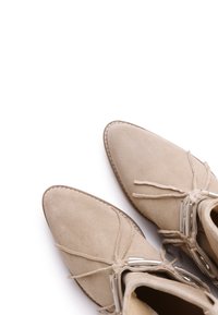 Beige suede ankle boots with a pointed toe, lace ties, and silver hardware accents. Smooth texture and visible stitching detail.