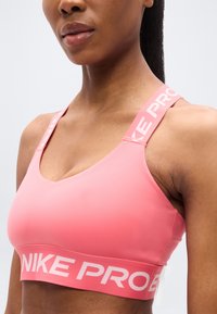 Ροζ αθλητικό σουτιέν με σχέδιο V-λαιμόκοψης, χοντρές τιράντες με το κείμενο "NIKE PRO" και λείο, ελαστικό ύφασμα.
