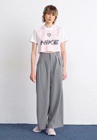 Rövidített fehér ing rózsaszín függőleges csíkokkal és fekete "NIKE" logóval, szürke csíkos széles lábú nadrággal párosítva.