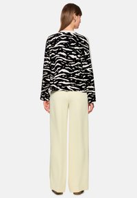 Black and white zebra-striped sweater with a relaxed fit, long sleeves, and round neckline, paired with high-waisted, wide-leg light yellow pants.