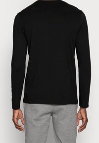 Zwart T-shirt met lange mouwen van katoen, met een klassieke ronde hals en een ontspannen fit, gecombineerd met grijze joggingbroeken.