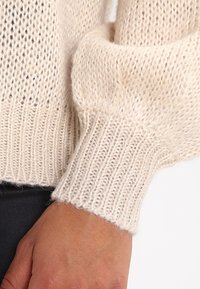 Ljust beige stickad tröja med ribbat mönster i ärmarna, breda ärmar, lös passform och mjukt material.