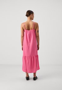 Ροζ, αμάνικο maxi φόρεμα με συγκεντρωμένο ντεκολτέ, πολυεπίπεδο τελείωμα και ρυθμιζόμενους ιμάντες, κατασκευασμένο από ελαφρύ ύφασμα.