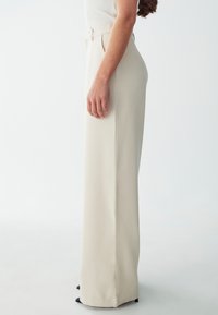 Beige high-waisted wide-leg trousers made of smooth fabric, featuring a side seam detail and a clean, structured silhouette.