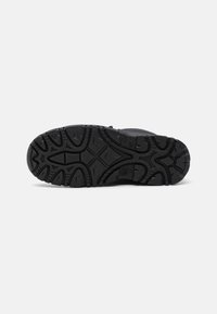 Suela de sneaker negra con un patrón texturizado que presenta surcos y relieves para tracción. Material de goma con diseños curvados y angulares.