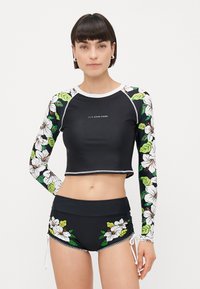 Black crop top with long sleeves featuring floral patterns and green leaves, paired with black shorts adorned with floral accents and drawstrings.