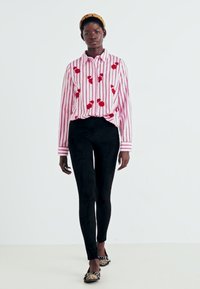 Chemise rayée rouge et blanche avec broderies florales, associée à des leggings noirs et des ballerines à motifs. Design simple et tissu léger.