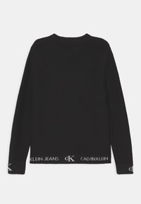 Czarny prążkowany sweter z długimi rękawami, z okrągłym dekoltem i dzianinową fakturą. Na dole znajduje się pasek z logo z napisem "CALVIN KLEIN JEANS."