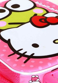 Roze rugzak met karakterontwerpen met een witte gezicht, zwarte accenten en een rode strik; gestructureerd oppervlak met polka dots en netzijde.