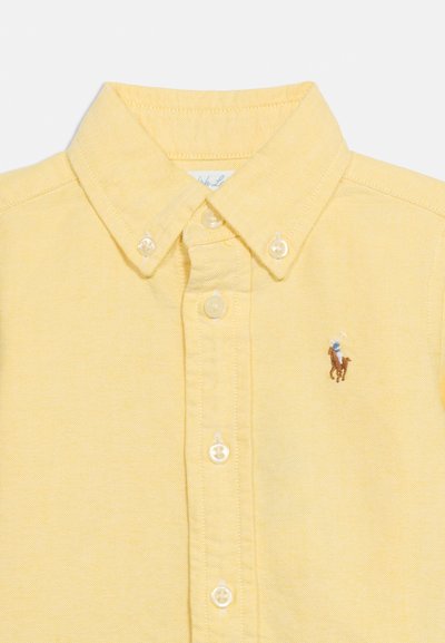 Camisa amarilla abotonada con cuello abotonado y pequeño logo bordado de un jugador de polo a caballo en el pecho izquierdo.