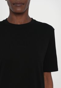 Czarny t-shirt z krótkim rękawem, wykonany z miękkiego materiału, z okrągłym dekoltem. Posiada subtelne wytłoczone logo na klatce piersiowej. Prosty i dopasowany krój.