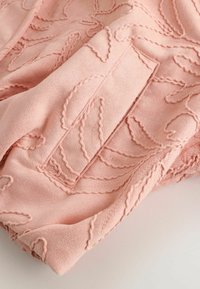 Tissu rose doux avec une broderie torsadée en relief formant des motifs abstraits de feuilles et un panneau rectangulaire cousu.