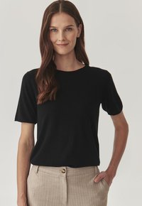 T-shirt nera a maniche corte con scollatura rotonda. Materiale morbido e liscio con una vestibilità rilassata, abbinato a pantaloni striati beige chiaro.