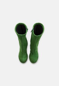 Bottes en suède vertes hauteur genou avec des zips sur les côtés extérieurs, bouts ronds et texture lisse.