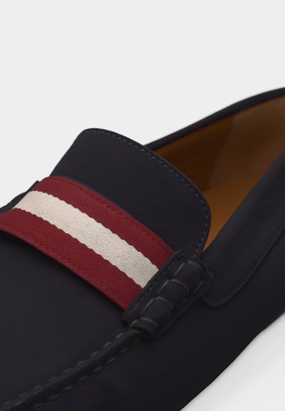 Mocassin bleu marine avec une bande en tissu rayée rouge et blanche sur le dessus, coutures visibles et doublure intérieure beige.
