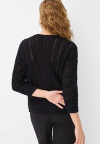 Schwarzer Strickpullover mit offenem Design, Dreiviertelärmeln und geripptem Saum. Die Textur ist leicht und atmungsaktiv.