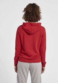 Czerwona bluza z kapturem o teksturowanej tkaninie, z rękawami raglanowymi i kieszenią kangurką, w zestawie z jasnoszarymi dresami.