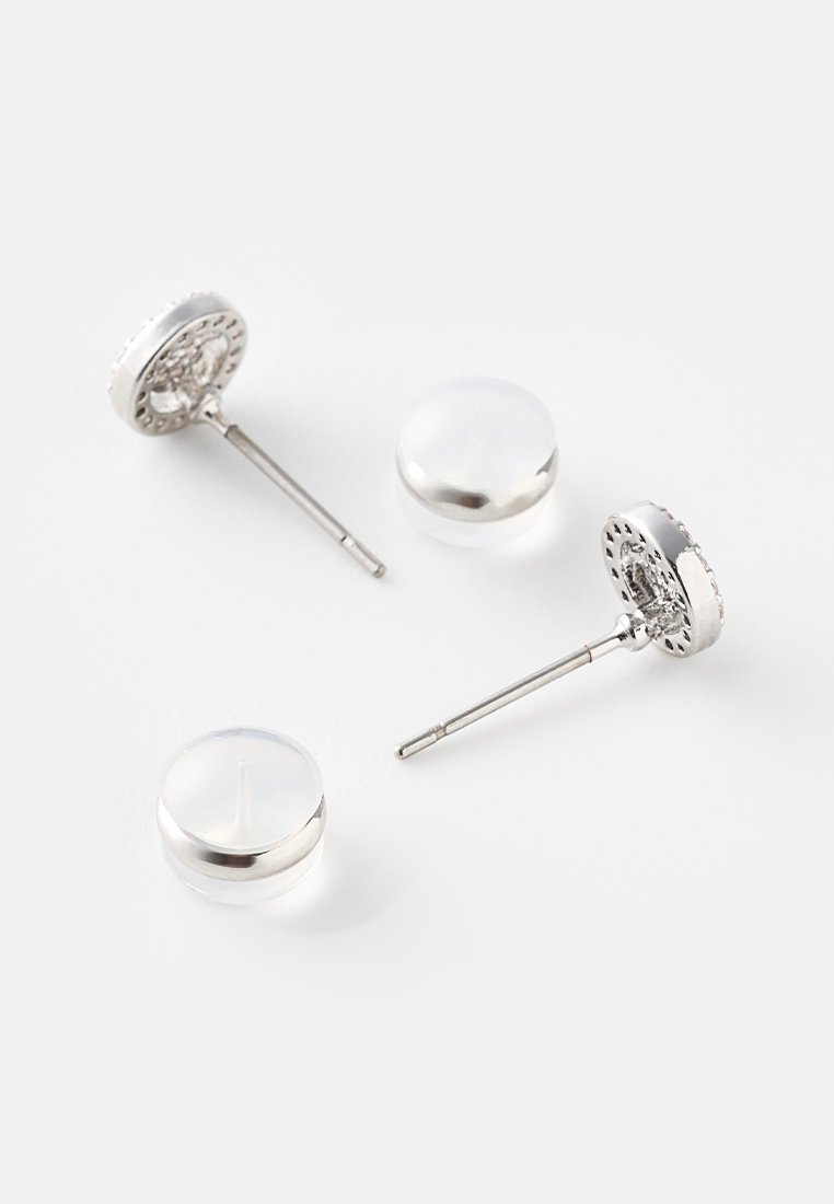 Orecchini a bottone in tonalità argento con design floreale in rilievo, dotati di pietre circolari trasparenti e perni in metallo. Superfici rotonde e lucide.