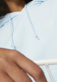 Lichtblauwe hoodie met een koord, voorzien van een geborduurd wit Puma-logo. Glossy stof en een relaxed fit met een grote capuchon.