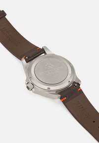 Boîtier de montre en acier inoxydable argenté avec un bracelet en cuir véritable marron. Présente des coutures oranges et un dos détaillé embossé avec "EXPEDITION NORTH TIMEX."