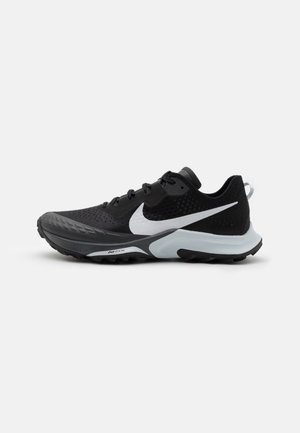 Chaussure de course Nike noire et blanche avec semelle texturée, logo Swoosh blanc et lacets noirs sur un fond clair uni.