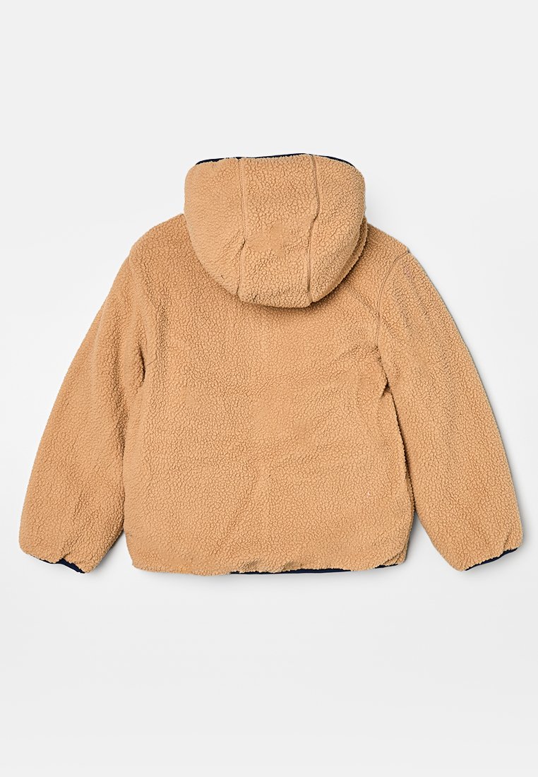 Veste en polaire beige avec capuche, présentant une texture douce, des poignets élastiques et un bord bleu marine le long de l'ourlet et des manches.
