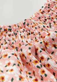 Pink stof med lille hvid, gul og bordeaux blomsterprint og samlet elastisk rynkedetalje.