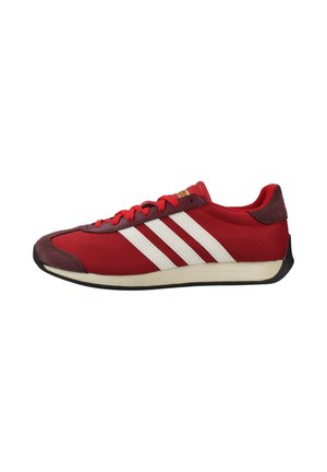 Zapatilla deportiva baja roja con rayas blancas de Adidas, cordones rojos, puntera de ante y suela negra.