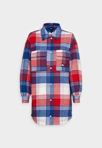 Camicia di flanella a quadri rossi, blu e bianchi con maniche lunghe, apertura con bottoni e due tasche frontali. Presenta un'etichetta con logo sulla tasca sinistra.