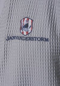 Gray textured fabric with a waffle weave. Features a shield logo with red and white stripes, and the text "JANVANDERSTORM" in dark blue.