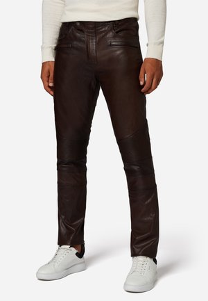 Brune læderbukser med en glat finish, der har ribbede detaljer på knæene og diskrete syninger. Sammen med hvide sneakers.