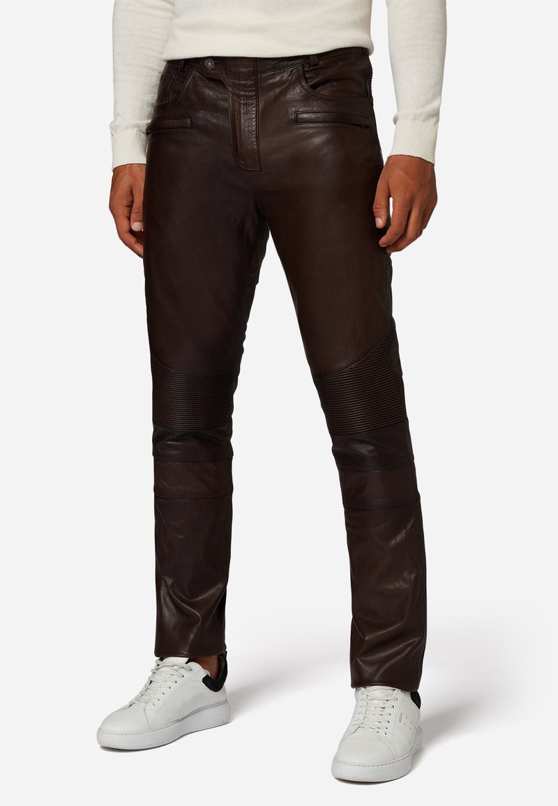Bruine leren broek met een gladde afwerking, voorzien van ribbelaccenten op de knieën en subtiele stikdetails. Gecombineerd met witte sneakers.