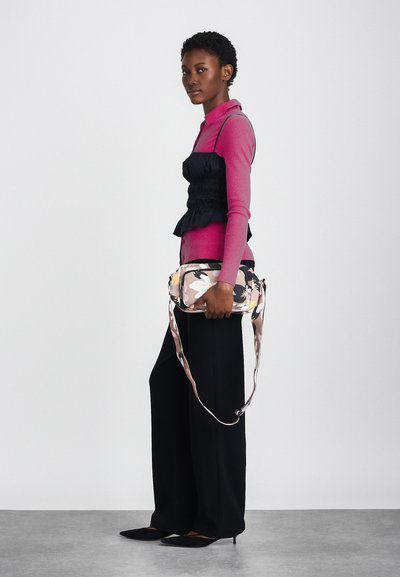 Černý krátký top, růžová košile s dlouhým rukávem, široké černé kalhoty a obdélníková taška s květinovým potiskem a dlouhým popruhem. Černé špičaté boty.