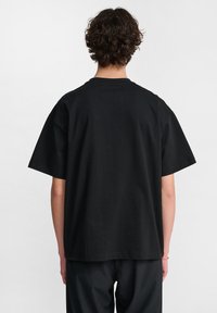 Czarna bawełniana koszulka z okrągłym dekoltem, krótkimi rękawami i luźnym krojem. Brak widocznych wzorów lub akcentów. Z tyłu gładka struktura.