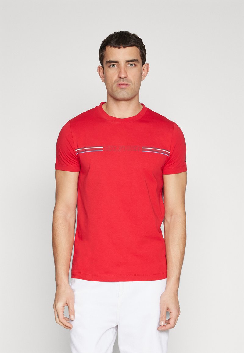 T-shirt in cotone rosso con maniche corte, colletto a girocollo e strisce decorative blu, bianche e rosse sul petto. Presenta un logo ricamato.