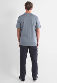T-shirt gris à manches courtes avec un col rond, associé à un pantalon cargo bleu marine foncé. Le T-shirt présente un petit logo sur l'épaule.