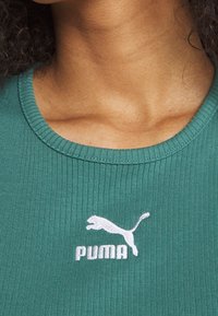 Zielony, prążkowany top z okrągłym dekoltem i białym haftowanym logo Puma pod kołnierzem.