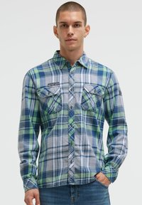 Blau-grün kariertes Flanellhemd mit zwei Brusttaschen, Button-Down-Kragen und sichtbaren Nähdetails. Getragen mit blauen Jeans.