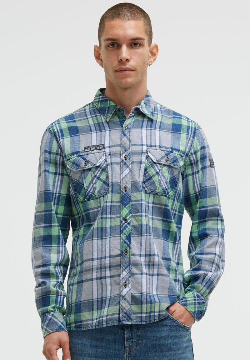 Blau-grün kariertes Flanellhemd mit zwei Brusttaschen, Button-Down-Kragen und sichtbaren Nähdetails. Getragen mit blauen Jeans.