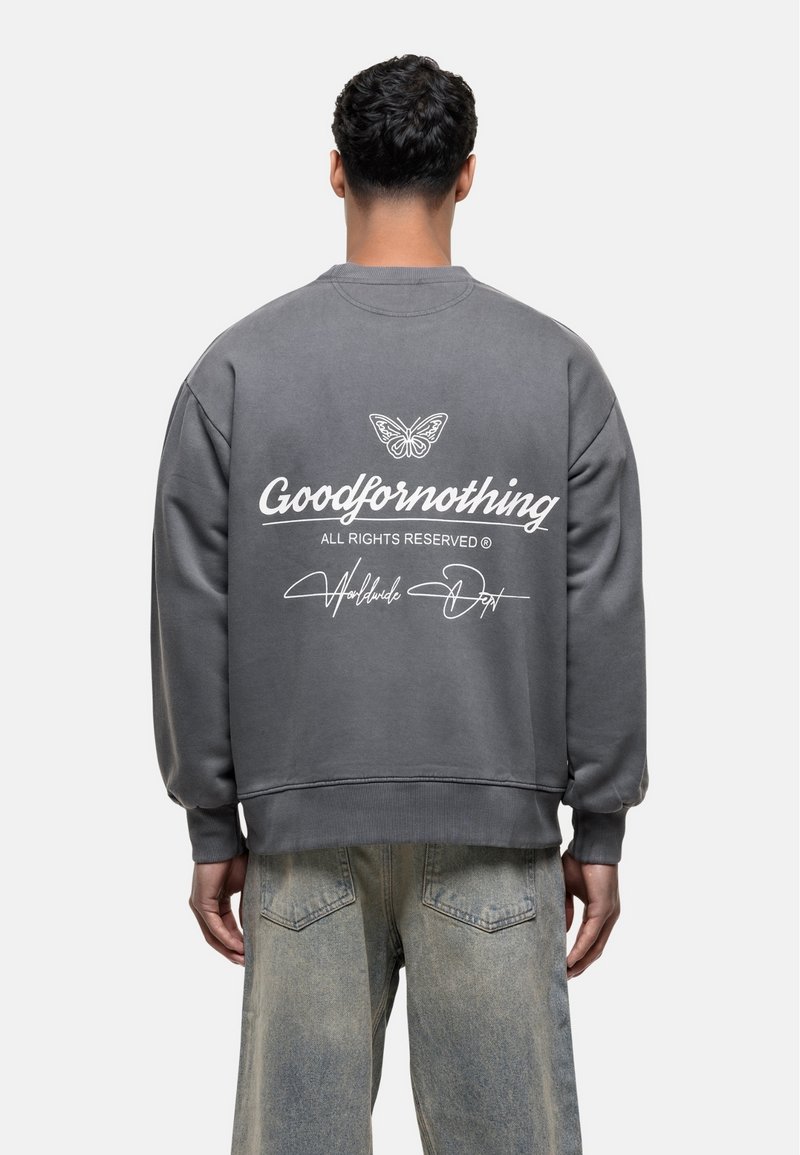 Grijze sweatshirt met een ronde hals en ribbels aan de mouwen. Heeft witte tekst en een vlinder graphic op de achterkant. Draagt het met licht afgewassen jeans.