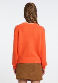 Maglione arancione lavorato a maglia con orlo e polsini a costine, caratterizzato da una vestibilità rilassata e una texture morbida. Abbinato a una gonna in camoscio marrone.