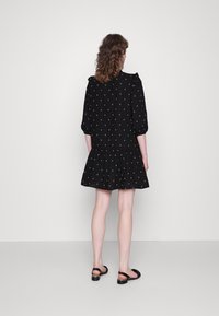 Vestido preto com padrão de bolinhas, mangas curtas e bufantes, bainha com babados, feito de tecido leve, combinado com sandálias pretas.