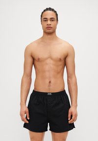 Μαύρα μαγιό με ελαστική μέση και λεπτομέρεια κουμπιού. Ελαφρύ ύφασμα με ομαλή υφή. Απλός σχεδιασμός, χωρίς επιπλέον μοτίβα.