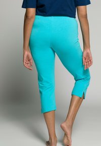 Akvové zkrácené legíny s elastickým pasem a bočními rozparky na lemu, vyrobené z měkké, elastické tkaniny, zobrazené zepředu.