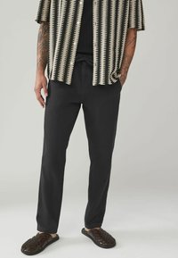 Pantaloni negri cu o croială ajustată, cu talie ajustabilă prin siret. Asociați cu o cămașă cu mânecă scurtă, modelată, și sandale închise, țesute.