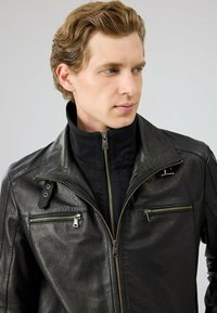 Zwarte leren jack met een hoge kraag, meerdere met rits afgesloten zakken en een gestructureerde afwerking met gouden hardware accenten.